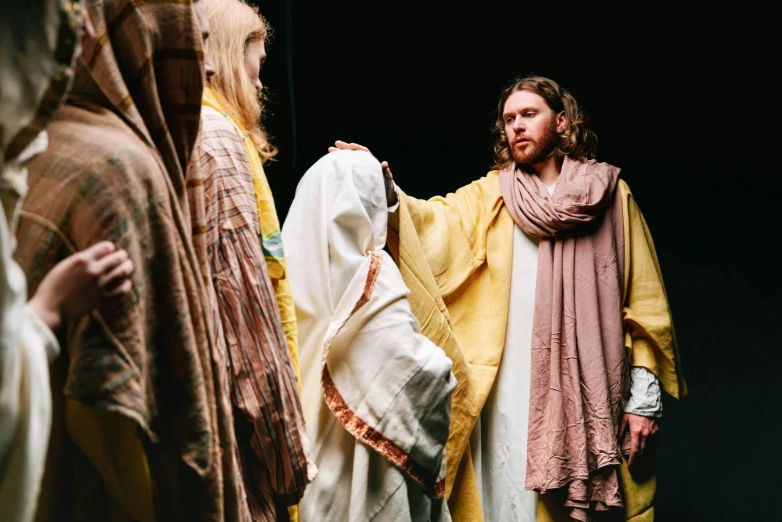 a group of people standing next to each other, unsplash, renaissance, dressed like jesus christ, several layers of fabric, yellow robe, ( ( theatrical ) )