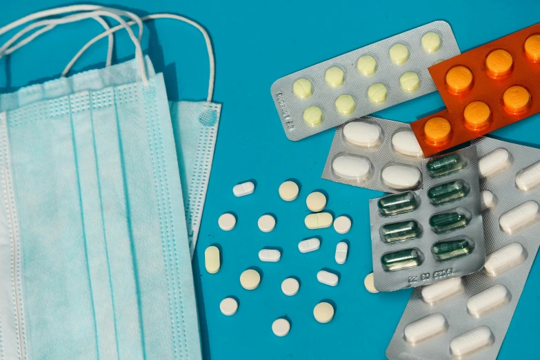 a bunch of pills and a face mask on a blue surface, plasticien, white and teal garment, on an operating table, high quality product image”, bandoliers