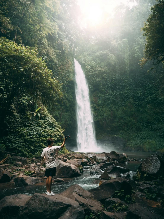 a man standing in front of a waterfall, pexels contest winner, sumatraism, overlooking, with a tall tree, good light, big island