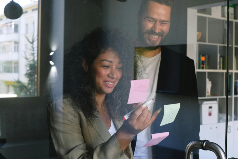 a man and a woman looking at post it notes, a photo, happening, near a window, avatar image, smiling, enes dirig