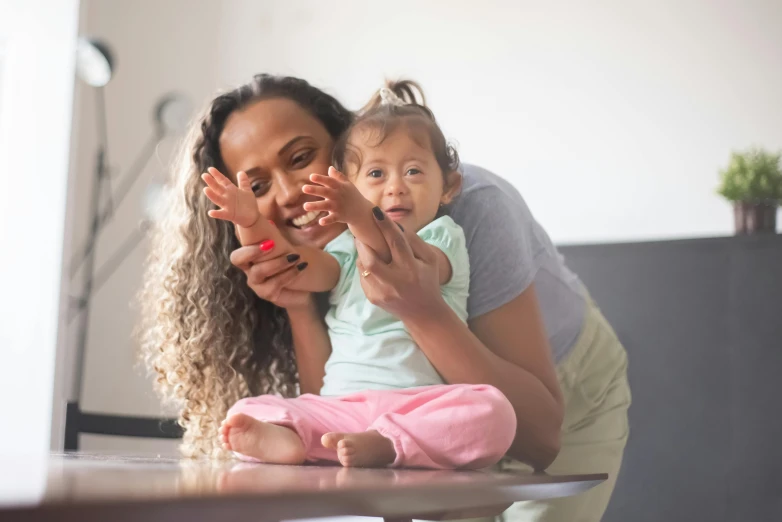 a woman holding a baby sitting on top of a table, pexels contest winner, mixed race, kid named finger, avatar image, high resolution photo