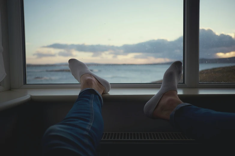 a person sitting on a window sill looking out at the ocean, slippers, plain stretching into distance, sitting in a lounge, manly