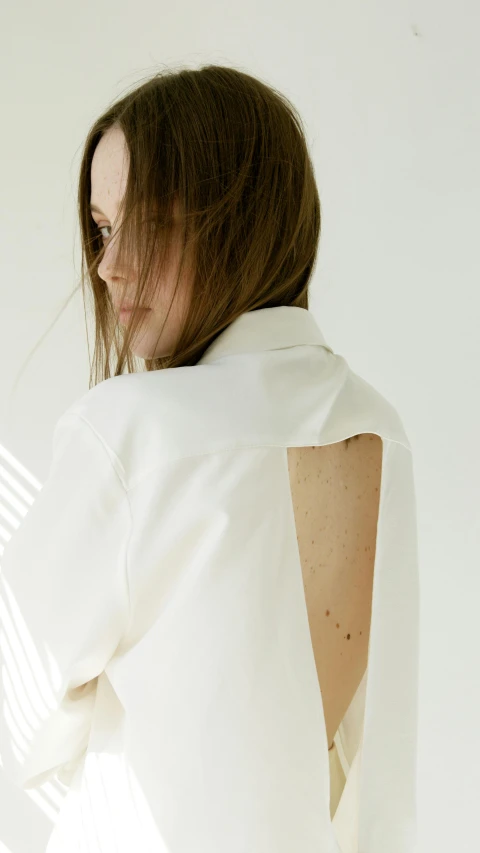 a woman standing in front of a white wall, an album cover, by Emily Shanks, trending on pexels, conceptual art, showing her shoulder from back, white blouse, detailed product image, kim hyun joo