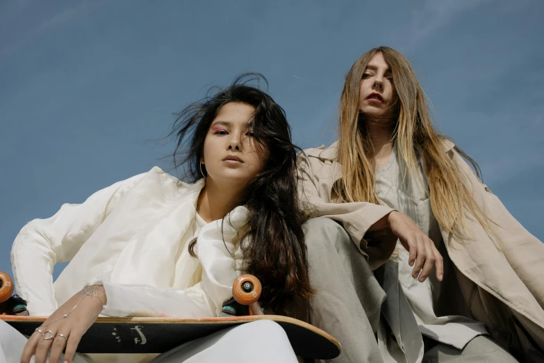 a couple of women sitting on top of a skateboard, trending on pexels, renaissance, flowing hair and long robes, uniform off - white sky, close - up photograph, magazine