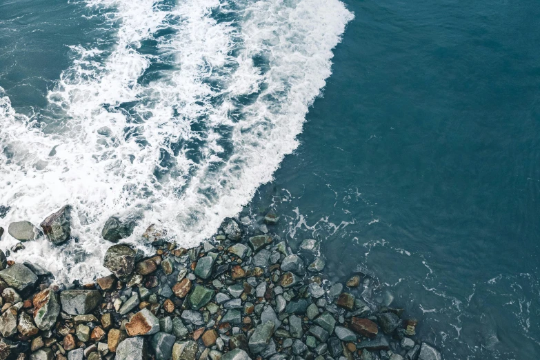 a person riding a surfboard on top of a rocky beach, pexels contest winner, minimalism, birdseye view, currents, sea foam, split in half