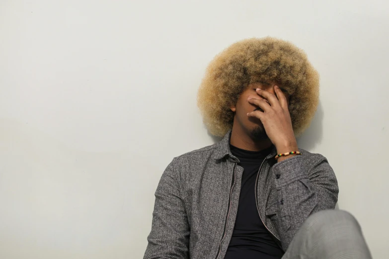 a man with an afro sitting against a wall, pexels, facepalm, human head with blonde hair, she is distressed, gray men