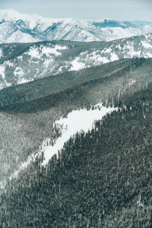 a man riding a snowboard on top of a snow covered slope, by Adam Marczyński, trending on unsplash, lush forest in valley below, aerial photo, grey, slightly pixelated