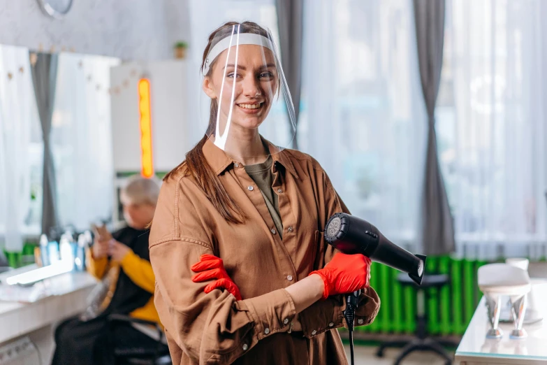 a woman in a hair salon holding a blow dryer, a portrait, by Julia Pishtar, pexels contest winner, wearing hi vis clothing, covered in transparent cloth, standing in class, brown