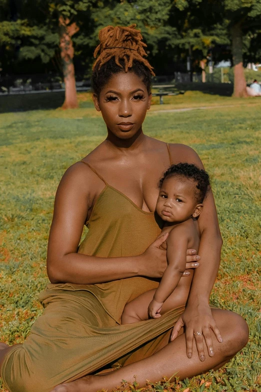 a woman sitting in the grass holding a baby, by Lily Delissa Joseph, muted colored bodysuit, willow smith young, sitting on a mocha-colored table, trending photo