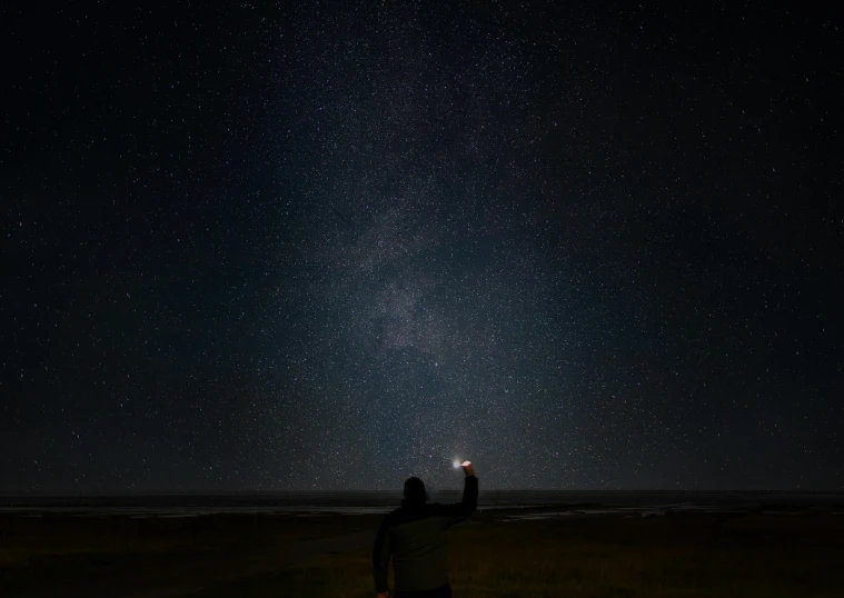 a man standing on top of a grass covered field under a night sky, pexels contest winner, minimalism, taking a selfie, holding a tiny galaxy, standing near the beach, pointing
