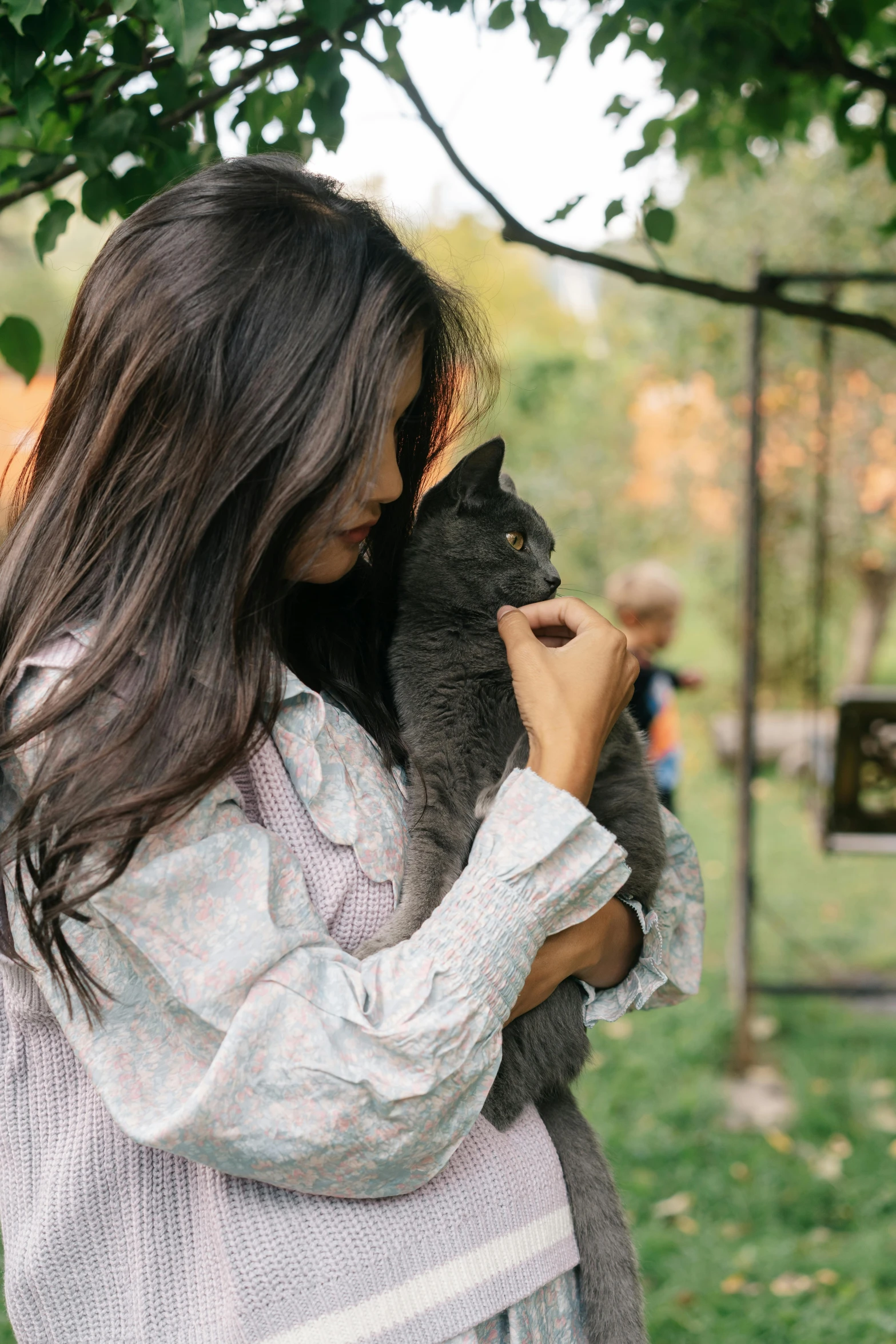 a woman holding a cat in a park, by Julia Pishtar, trending on unsplash, long thin black hair, mai anh tran, 256435456k film, handsome
