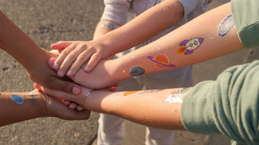 a group of people putting their hands together, a tattoo, solar punk product photo, rainbow coloured rockets, medium close shot, standing in the solar system