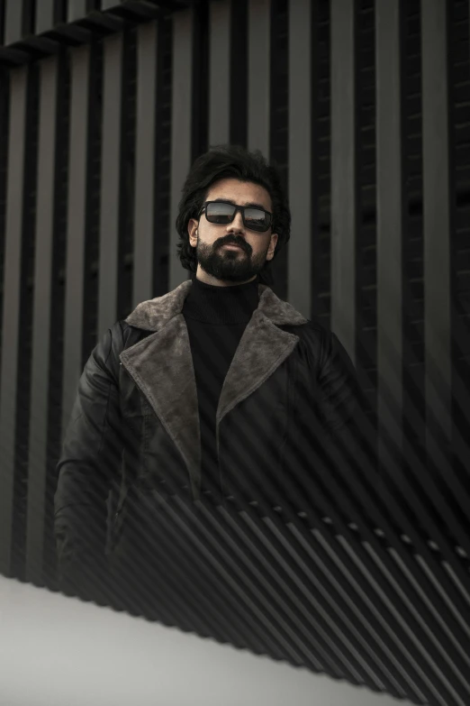 a man standing in front of a metal wall, an album cover, inspired by Germán Londoño, pexels contest winner, hurufiyya, wearing mirrored sunglasses, with a beard and a black jacket, escher mc, desaturated
