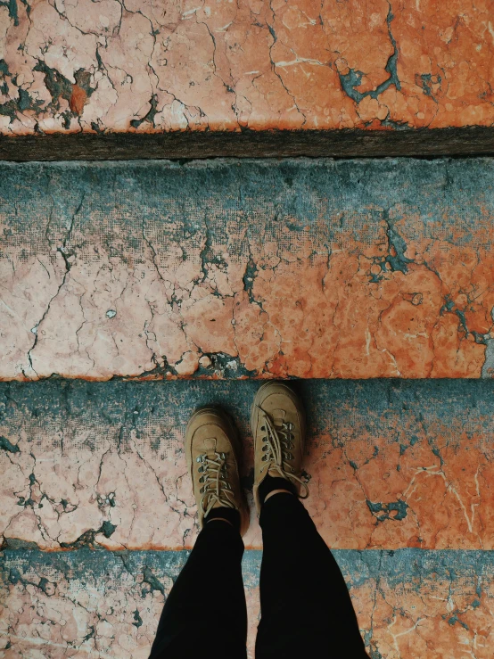 a person standing in front of a brick wall, inspired by Elsa Bleda, pexels contest winner, old stone steps, jean and multicolor shoes, ((rust)), floor tiles