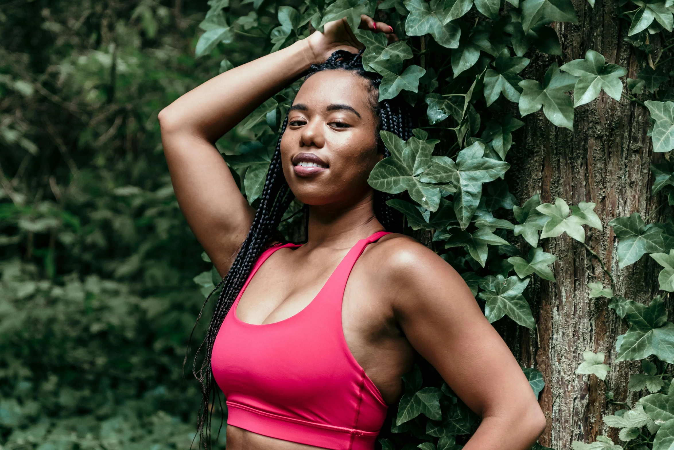 a woman in a pink sports bra top leaning against a tree, by Dulah Marie Evans, pexels contest winner, hurufiyya, covered in plants, red sport clothing, official product photo, mixed-race woman