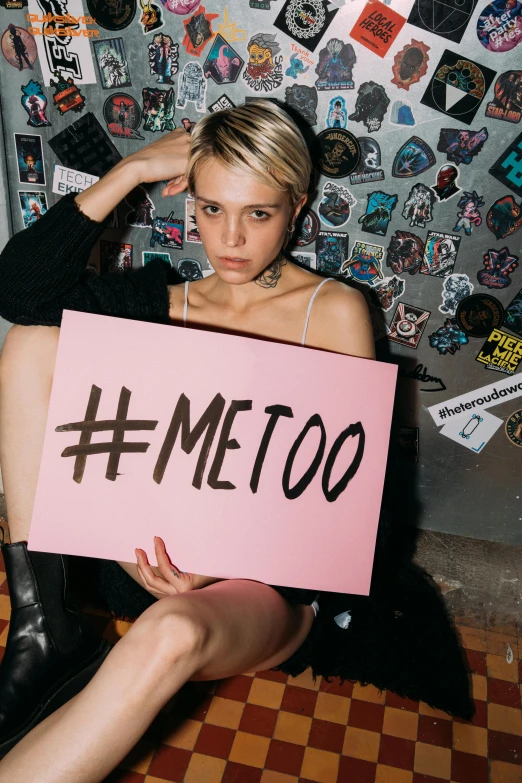 a woman sitting on the floor holding a sign, an album cover, inspired by Elsa Bleda, trending on pexels, feminist art, xxxtentacion, cara delevingne standing, gq magazine cover, metro