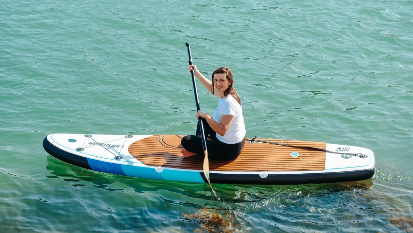 a woman sitting on a paddle board in the water, seraphine, accompanying hybrid, mickael lelièvre, sunny day