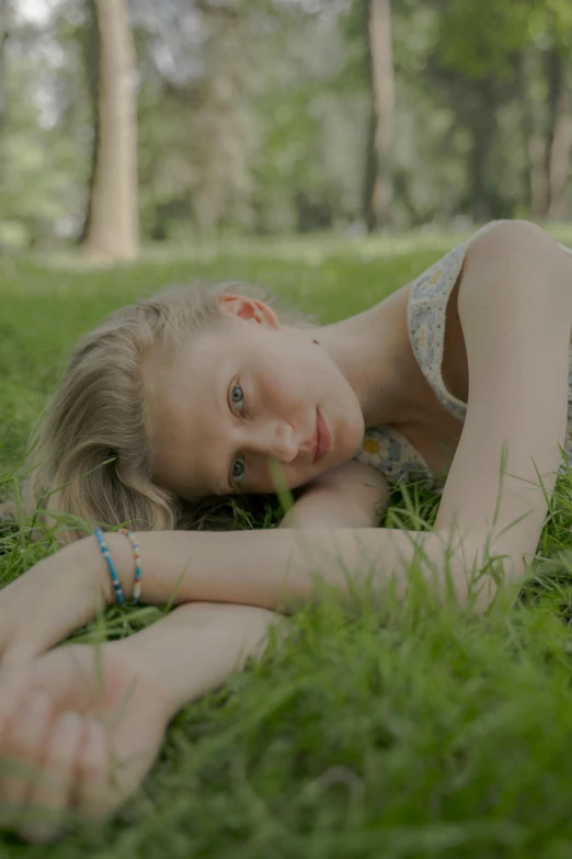 a young girl laying on top of a lush green field, a picture, inspired by Elsa Bleda, unsplash, a blond, portrait. 8 k high definition, ignant, in a city park