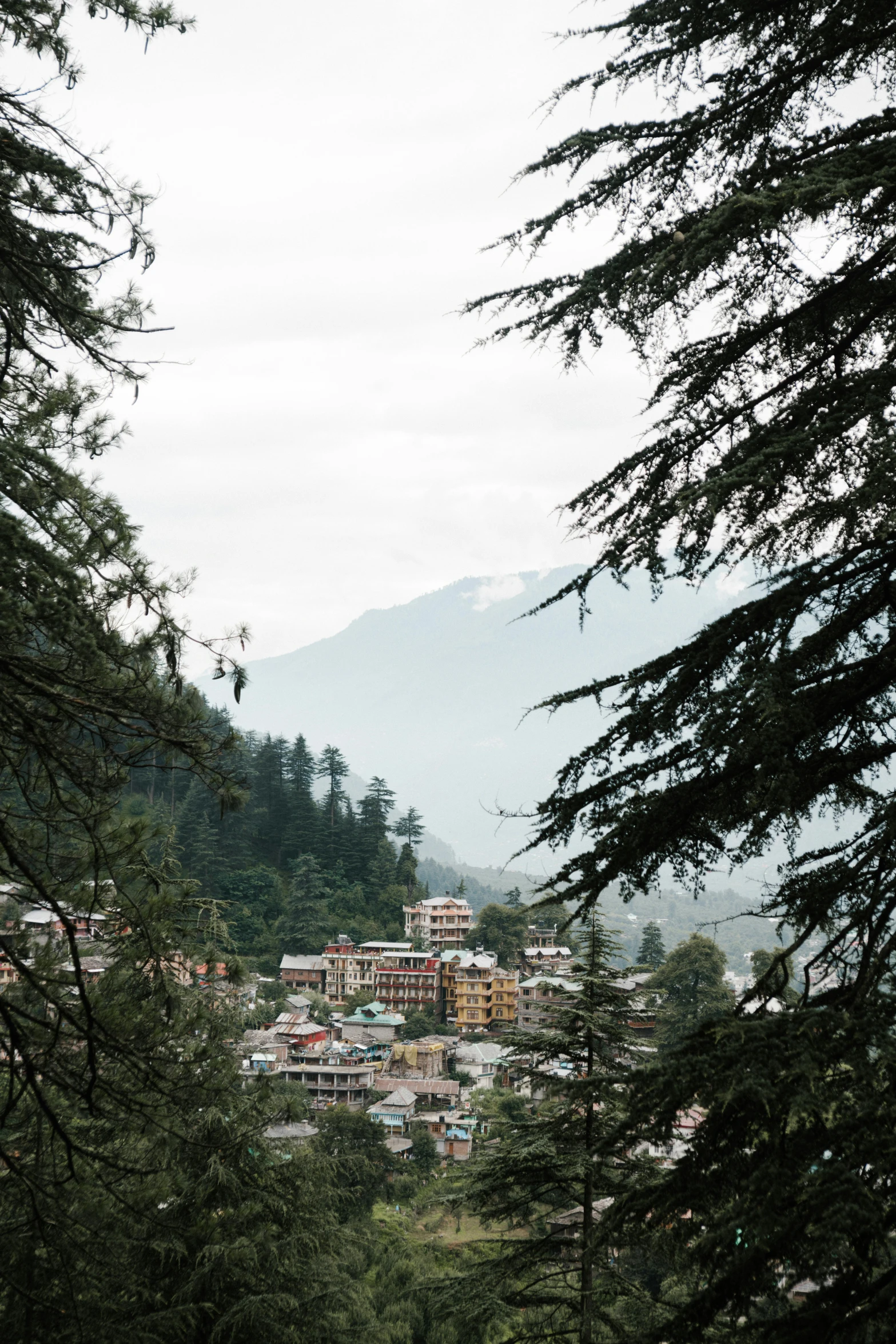 a view of a town through some trees, trending on unsplash, breathtaking himalayan landscape, square, grayish, slightly pixelated