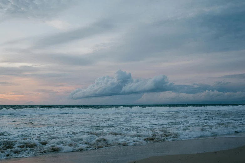 a man standing on top of a beach next to the ocean, by Ryan Pancoast, unsplash contest winner, layered stratocumulus clouds, overcast dusk, australian beach, cresting waves and seafoam