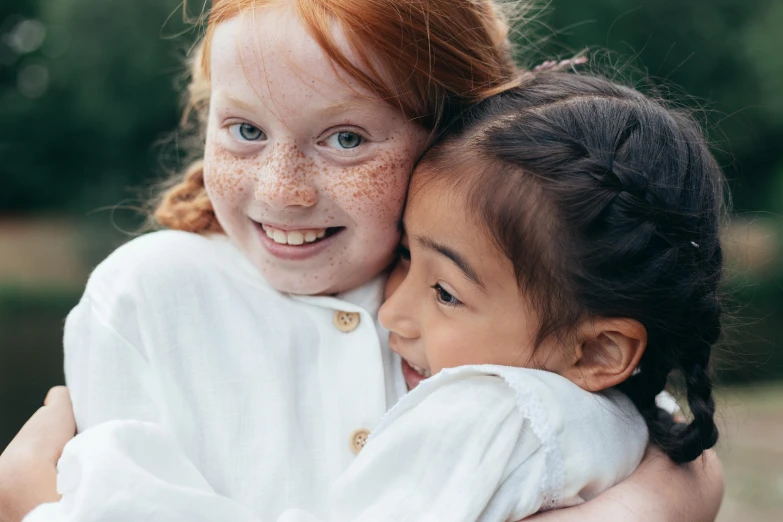 a close up of two children hugging each other, inspired by Sophie Anderson, pexels contest winner, ginger hair with freckles, asian girl, varying ethnicities, smiling girl