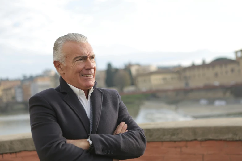 a man in a suit standing with his arms crossed, by Francesco Filippini, pexels contest winner, renaissance, river in front of him, daniel libeskind, giorgetto giugiaro, looking happy