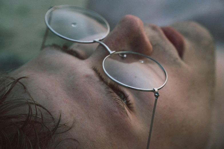 a close up of a person with glasses on, inspired by Elsa Bleda, lying down, silver silver glasses, sad man, upside down stranger things