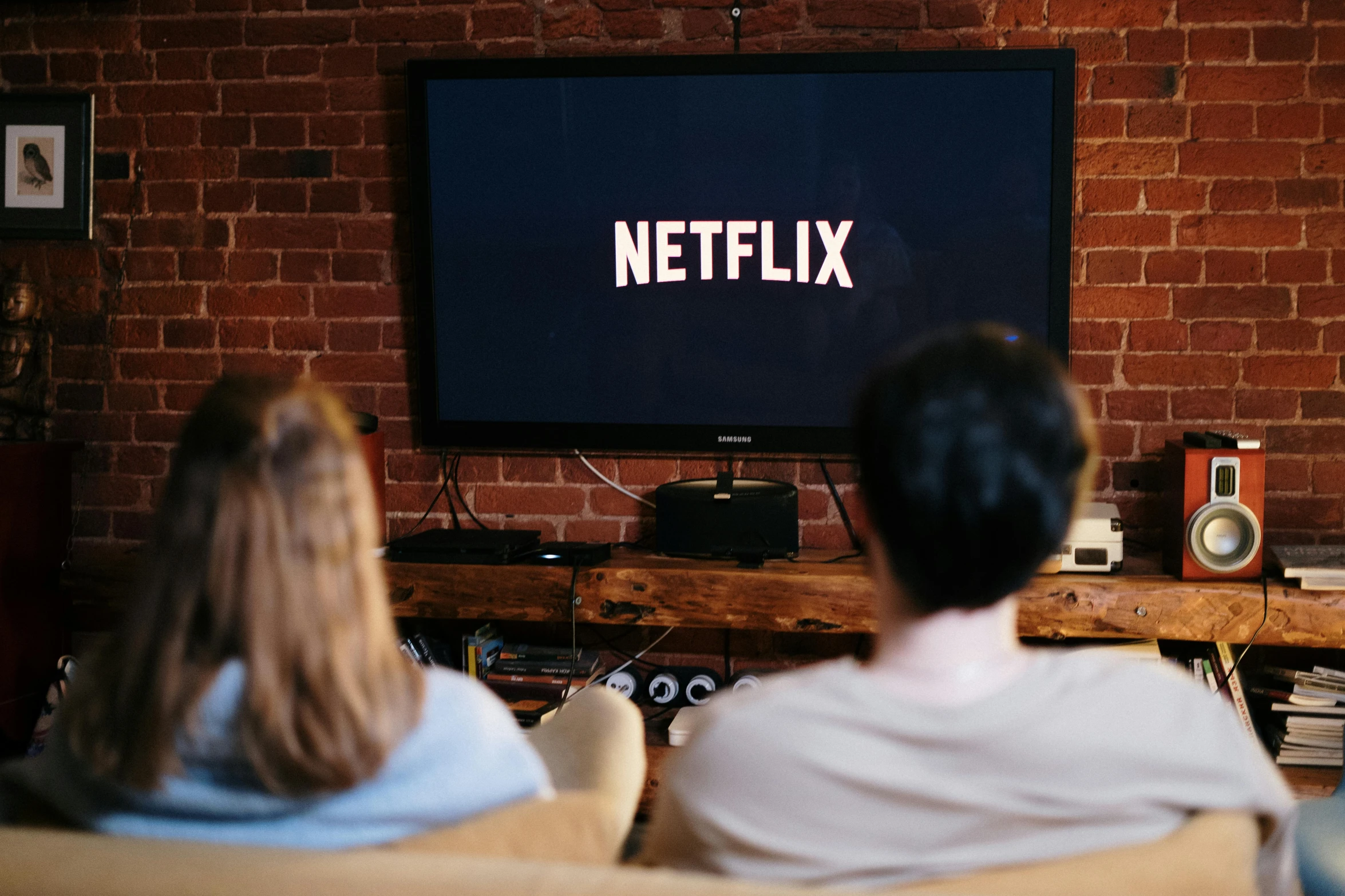 a man and a woman sitting on a couch in front of a television, pexels, serial art, netflix logo, close-up shot taken from behind, casual game, instagram post