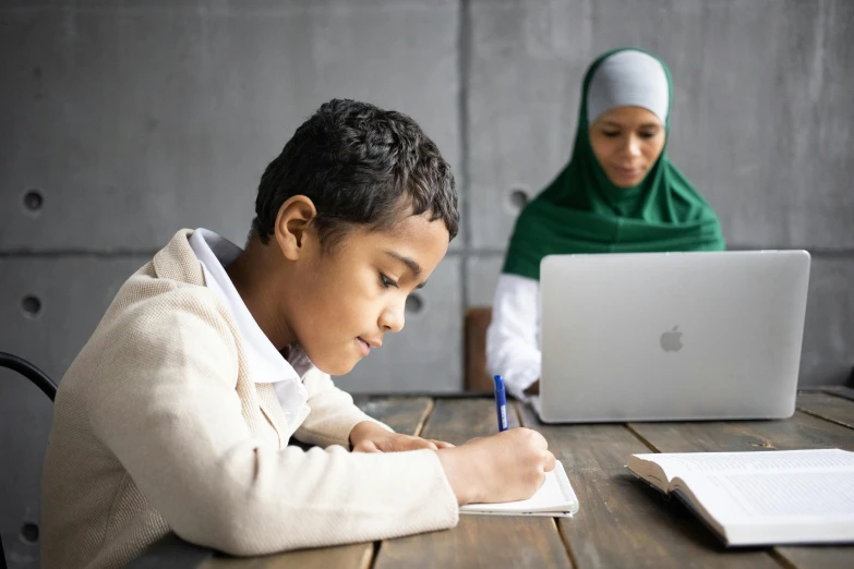 a young boy sitting at a table in front of a laptop computer, by Daren Bader, pexels contest winner, hurufiyya, teaching, ameera al taweel, alana fletcher, with apple