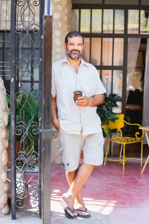 a man that is standing in front of a building, inspired by Germán Londoño, tan skin a tee shirt and shorts, patio, celebration of coffee products, linen