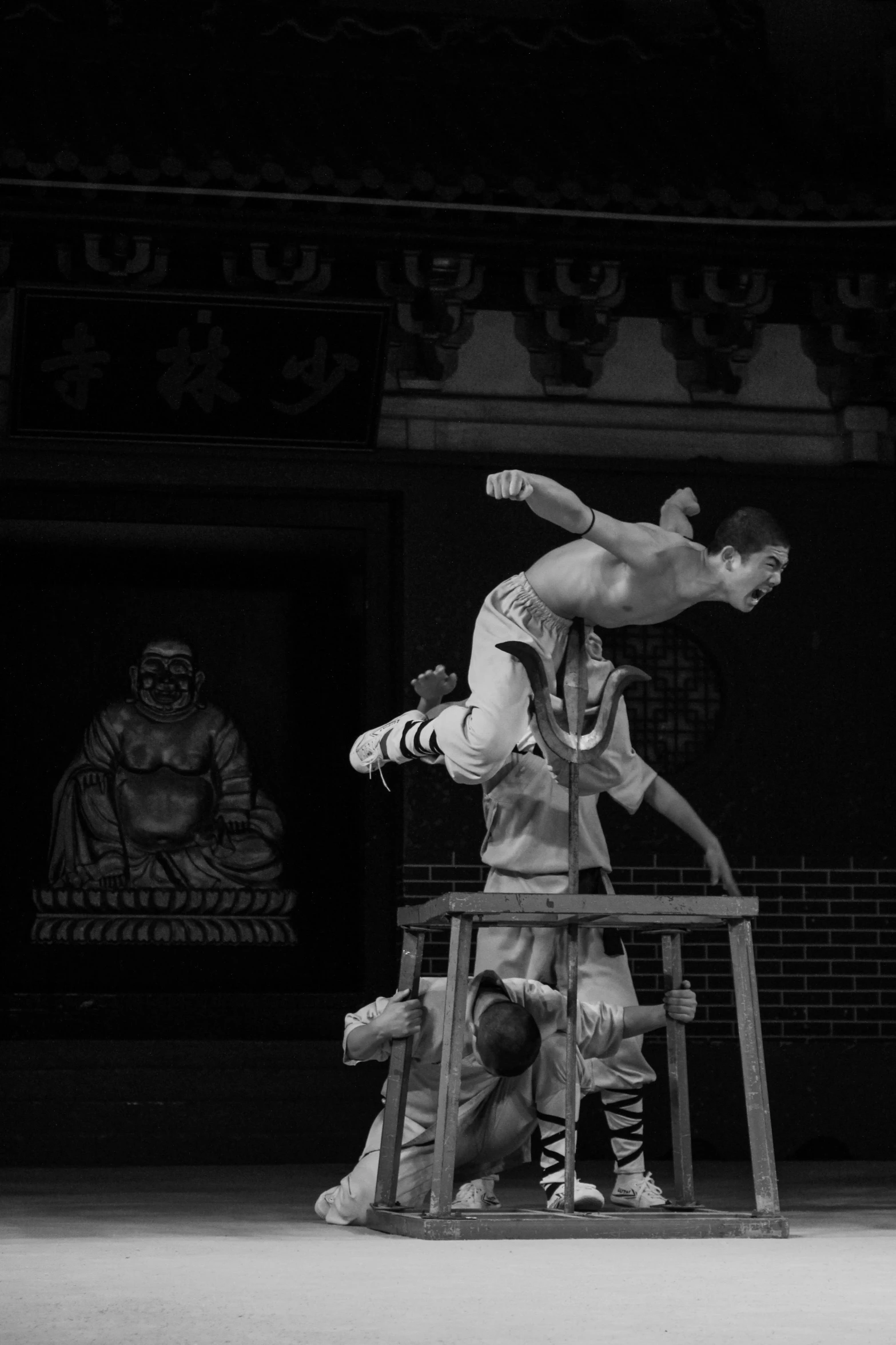 a black and white photo of a man doing a trick on a stool, inspired by Ma Quan, in a temple, monochrome:-2, world, temple fair