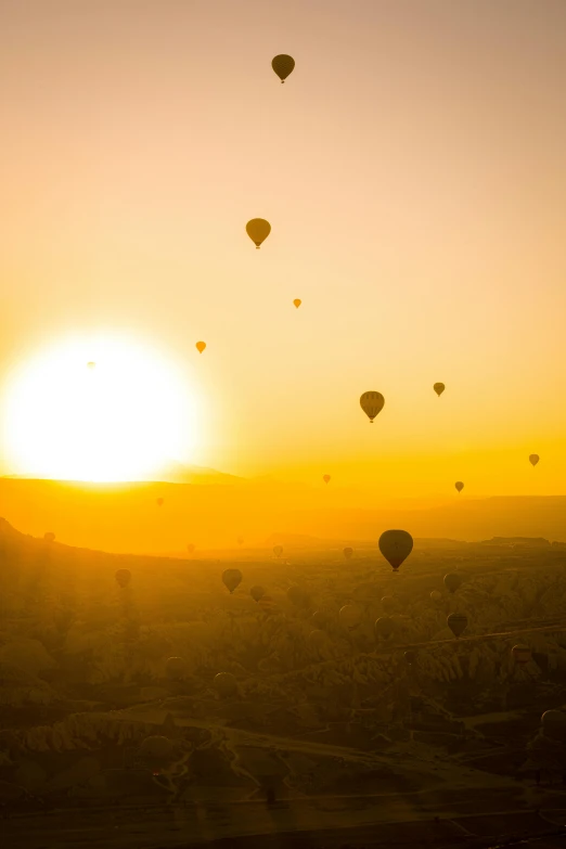 a group of hot air balloons flying over a city, by Daren Bader, pexels contest winner, happening, sunset in a valley, yellow, turkey, sun flares