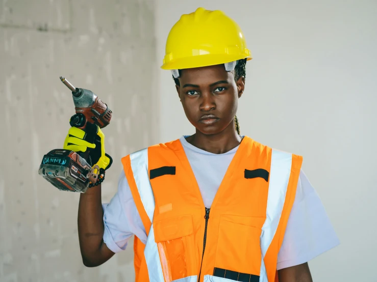 a woman in an orange safety vest holding a drillet, by Carey Morris, pexels contest winner, afro tech, holding a hammer, androgynous male, frontal pose