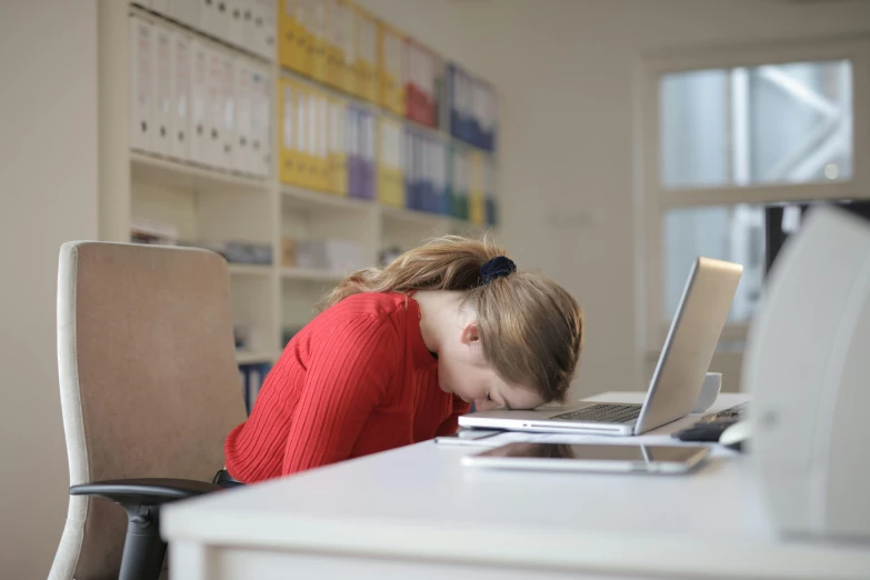 a woman sitting at a desk in front of a laptop computer, by Alice Mason, pexels, sleeping, face down, crimson themed, schools