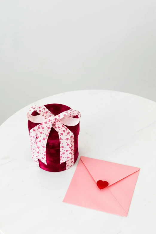 a present sitting on top of a table next to a pink envelope, red velvet, detailed product image, small stature, at home