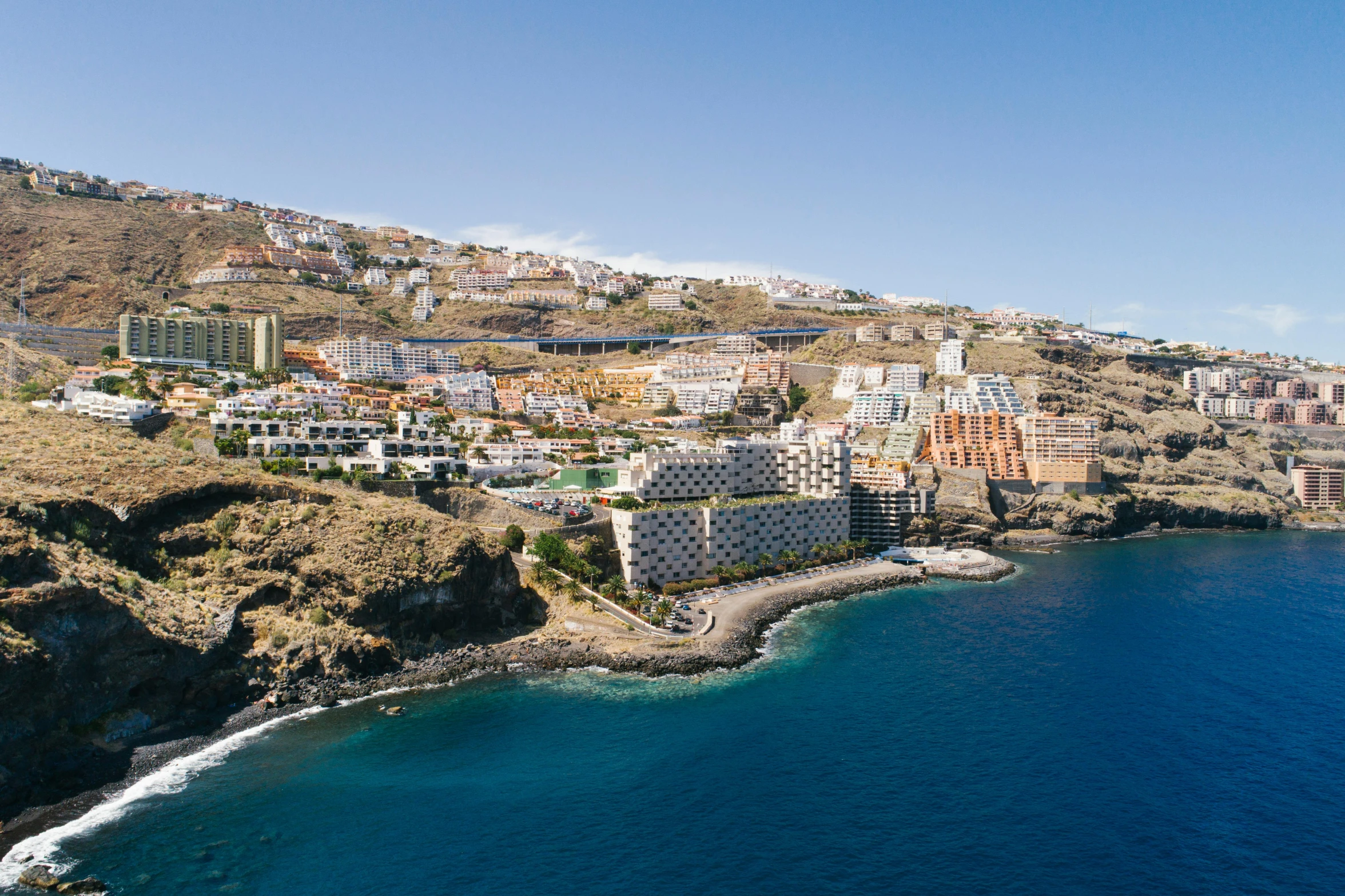 a large body of water next to a lush green hillside, by Daniel Lieske, pexels contest winner, whitewashed buildings, barcelo tomas, photo of the middle of the ocean, brown