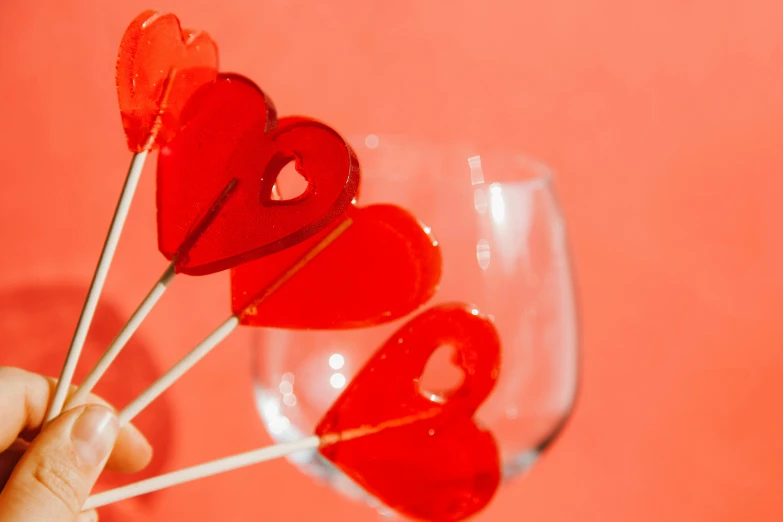 a person holding a bunch of heart shaped lollipops, by Julia Pishtar, pexels contest winner, wine glass, red theme, caramel, edible