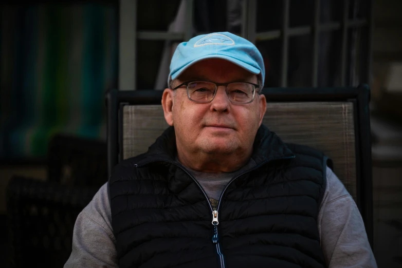 a man sitting in a chair wearing a blue hat, man with glasses, bill dauterive, humans of new york, profile image