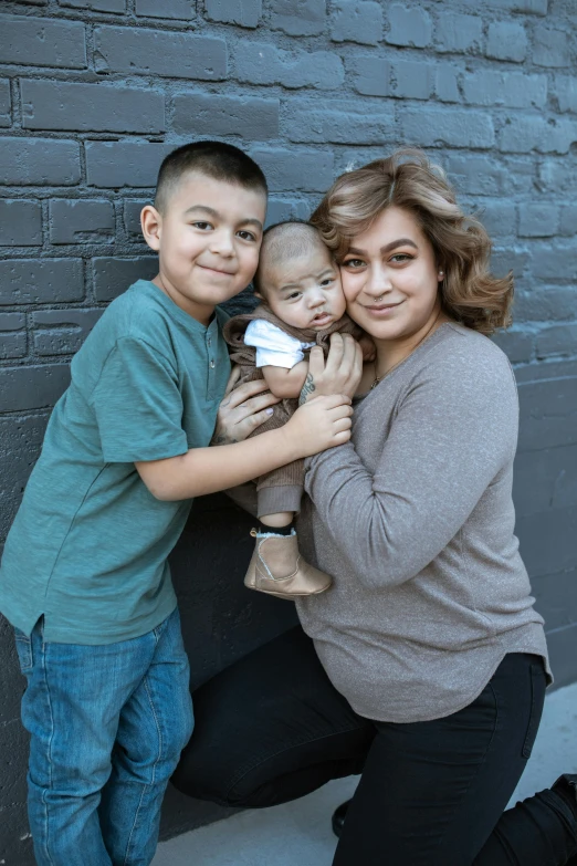 a family poses for a picture in front of a brick wall, a portrait, by Edward Avedisian, unsplash, transgender, migrant mother, square, cute boys