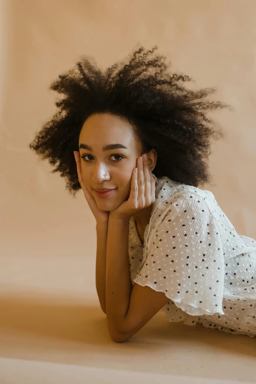 a beautiful young woman laying on top of a bed, a portrait, trending on pexels, ashteroth, on a pale background, sitting on a mocha-colored table, curly black hair