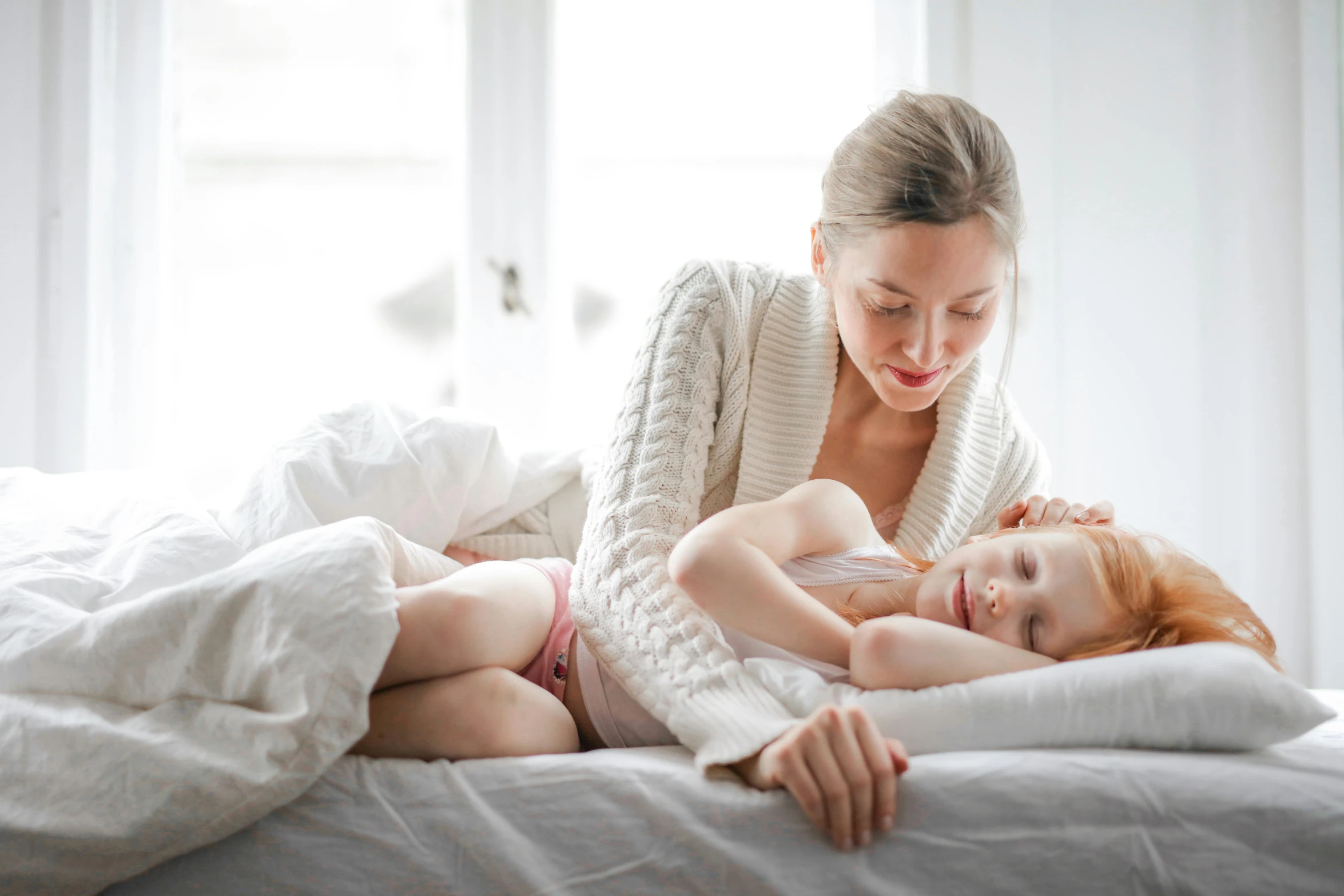 a woman laying on top of a bed next to a child, pexels contest winner, clean design, manuka, profile image, white