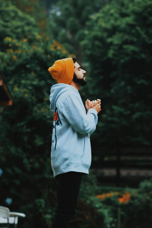 a man standing on top of a lush green field, an album cover, pexels, orange hoodie, pray, wearing beanie, avatar image