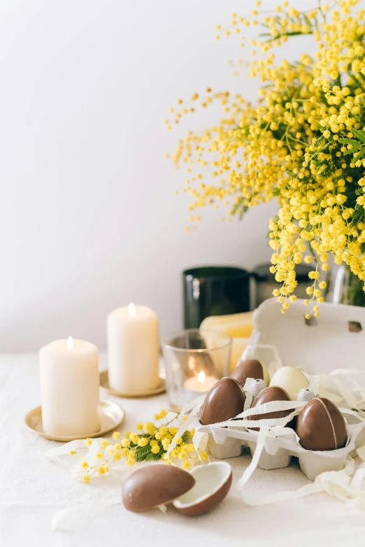 a bunch of eggs sitting on top of a table, white candles, with yellow flowers around it, chocolate, australian