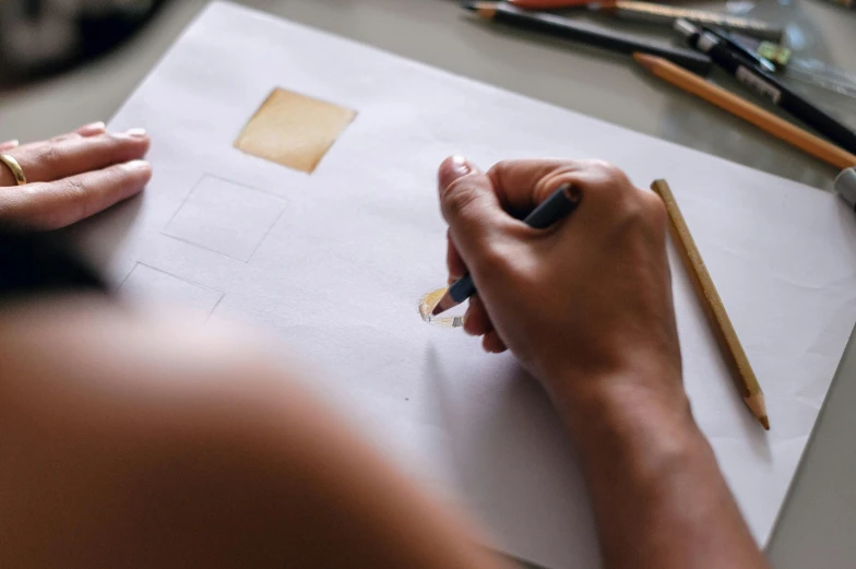 a person drawing on a piece of paper with a pencil, by karolis strautniekas, trending on pexels, arbeitsrat für kunst, square shapes, gold paint, handcrafted, professional image