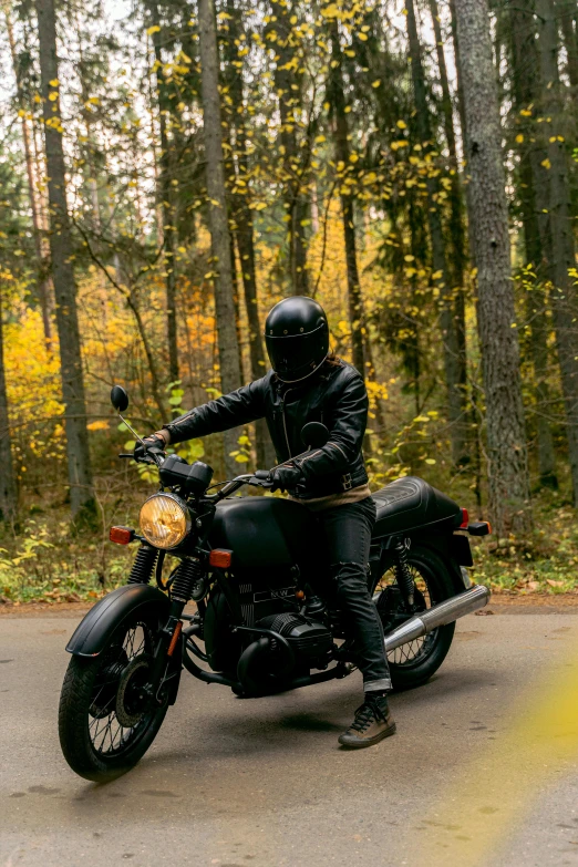 a man riding on the back of a motorcycle down a road, by Jaakko Mattila, unsplash, in serene forest setting, black armor with yellow accents, 2 5 6 x 2 5 6 pixels, during autumn