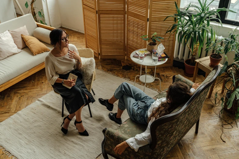 two women sitting on a couch in a living room, by Emma Andijewska, pexels contest winner, wide high angle view, giving an interview, comfy chairs, full body within frame