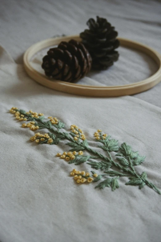 a couple of pine cones sitting on top of a table, a cross stitch, inspired by Master of the Embroidered Foliage, trending on unsplash, yellow robe, detail shot, cotton fabric, made of wildflowers