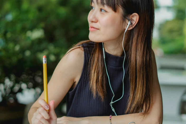 a woman sitting at a table with a pencil in her hand, trending on pexels, earbuds, portrait of a japanese teen, realistic »