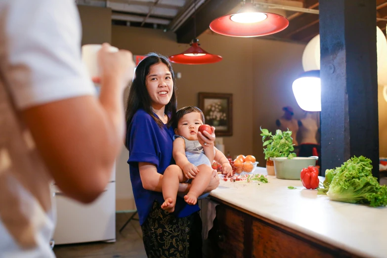 a woman holding a baby standing in front of a counter, pexels contest winner, zeen chin and farel dalrymple, ready to eat, bao pham, light from right