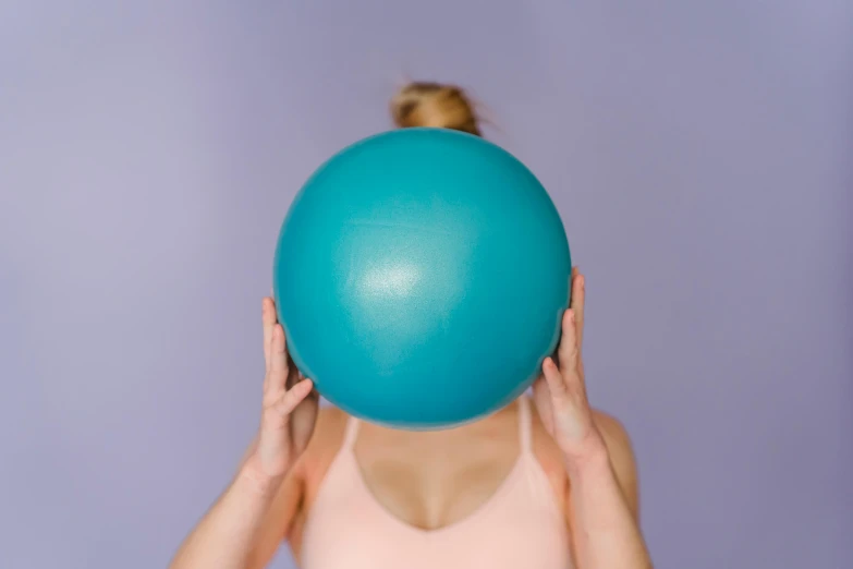 a woman holding a blue ball in front of her face, trending on pexels, mauve and cyan, with abs, tall forehead, bendover posture